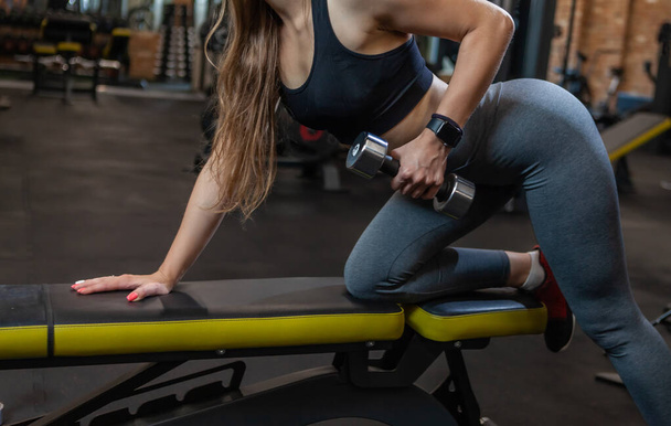 Beauty Woman bodybuilder in gym lifting dumbbells on bench at modern gym - Foto, Bild