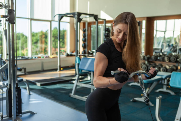 Mladá fit žena s dokonalým tělem ve sportovním oblečení vlaky biceps v crossover kabelové cvičení stroj v moderní tělocvičně - Fotografie, Obrázek