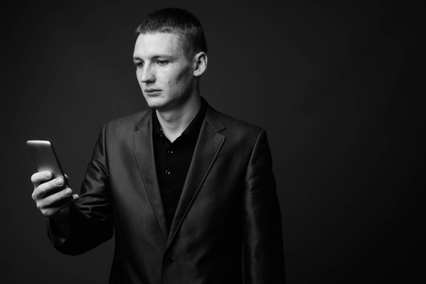 Studio shot of young businessman using mobile phone against brown background - Zdjęcie, obraz