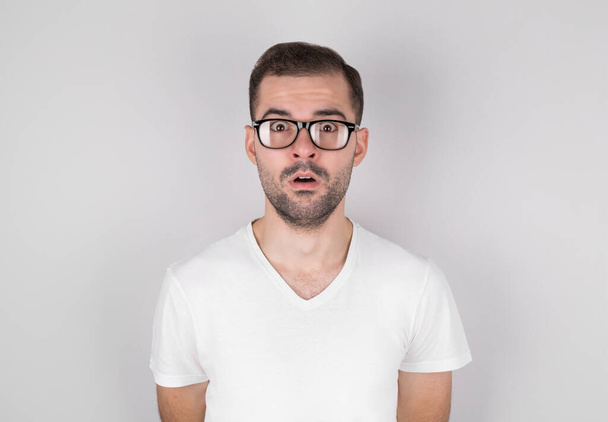 Surprised man in eyeglasses wearing white undershirt over grey background - Fotó, kép