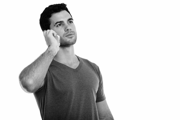 Studio shot of young handsome Hispanic man talking on mobile phone while thinking - Foto, Imagen