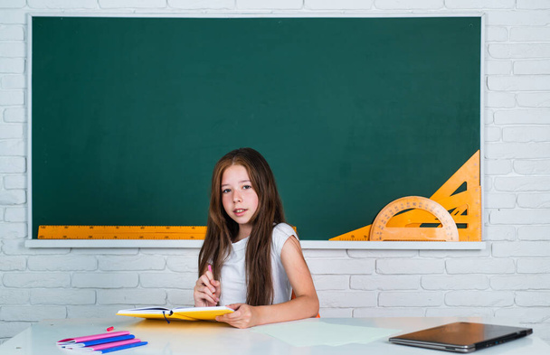 back to school. teen girl work in classroom near blackboard. cheerful kid learning subject. modern education. knowledge day. child pupil sit at table. girl is college student - Fotografie, Obrázek