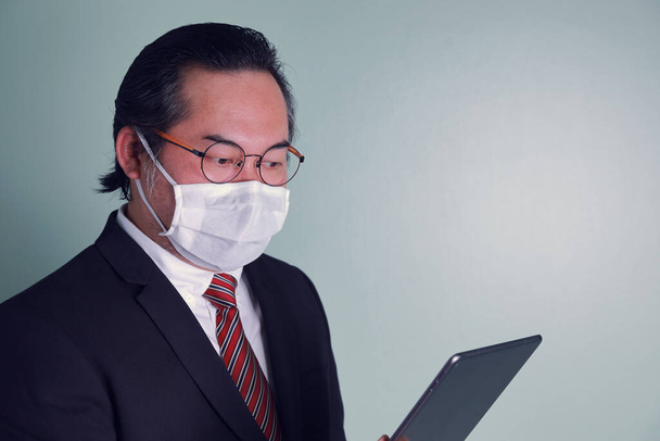 Портрет дорослого азіатського бізнесмена, одягненого в медичну маску, дивиться відео-дзвінок. Концепція: ділові люди охороняють коронавірус пандемії.. - Фото, зображення