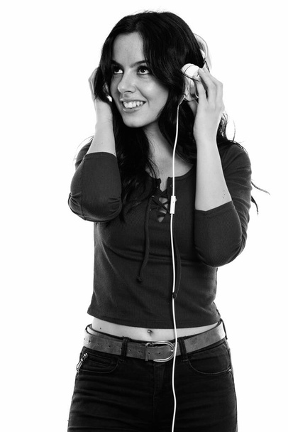 Studio shot of young happy Spanish woman smiling and thinking while listening to music - Foto, Imagen