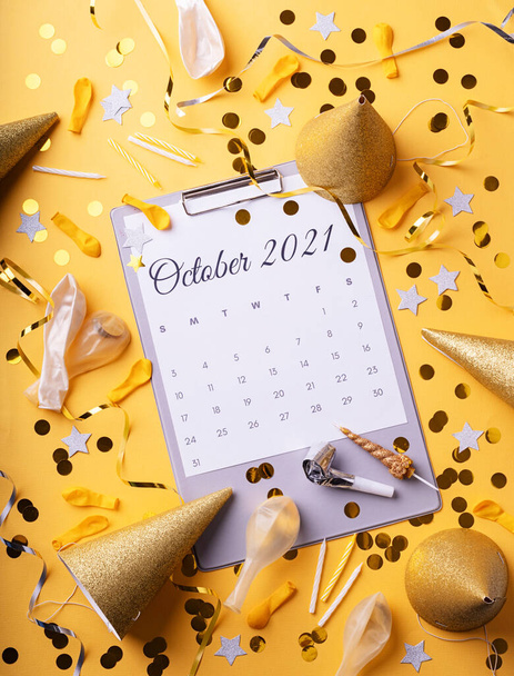 Październik 2021 kalendarz z konfetti, kapelusze urodzinowe, świece i balony widok z góry płaski leżał na żółtym tle. Kolory roku 2021 - Zdjęcie, obraz