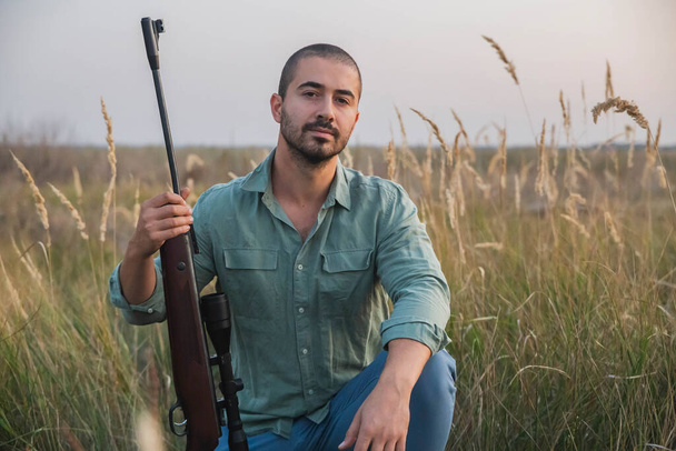 Hunter egy mesterlövész puskával ül a mezőn naplementekor. - Fotó, kép