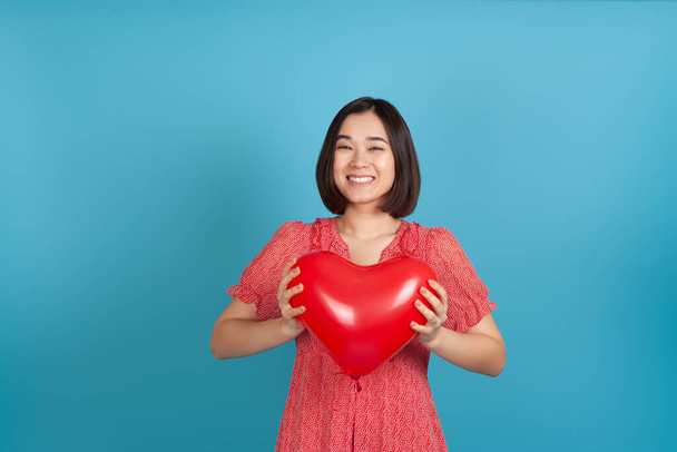 mock up laughing satisfied Asian woman holding red heart shaped balloon on Valentines day isolated on blue background - Fotografie, Obrázek