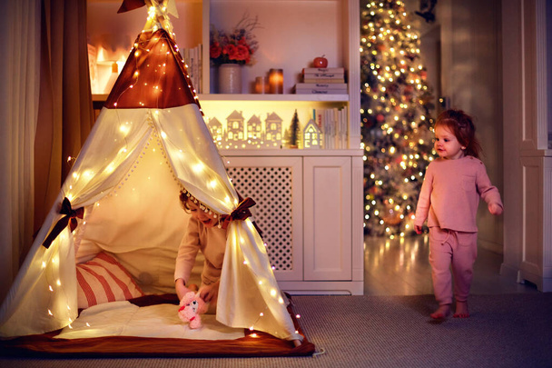 cute siblings, babies in pajamas playing in teepee tent at home in the evening on Christmas holidays - Zdjęcie, obraz