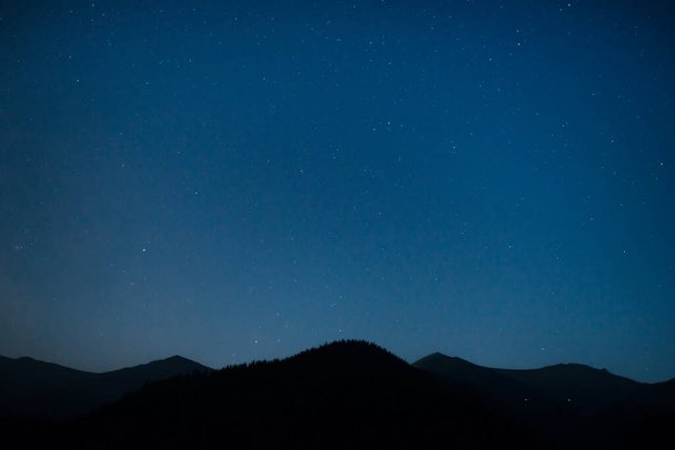 Силуэт горного хребта под темно-синим ночным небом со многими яркими звездами - Фото, изображение
