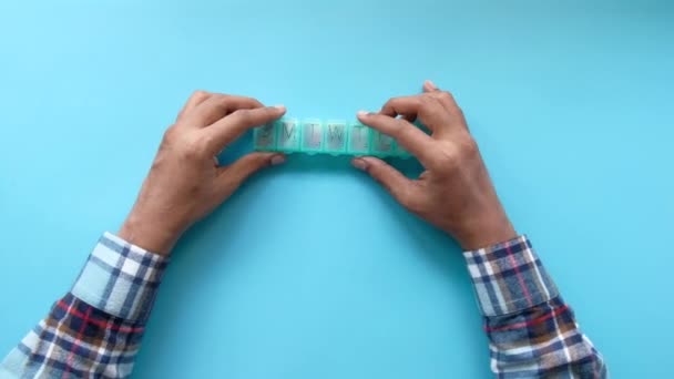 Vista superior de las manos del hombre tomando la medicina de una caja de pastillas sobre fondo azul  - Imágenes, Vídeo