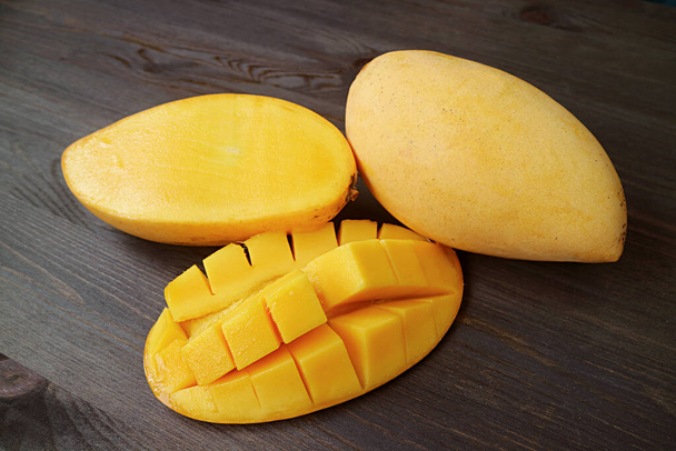 Fresh Ripe Mango Cut in Half and Crosswise Cut with a Whole Fruit on Black Wooden Background - Photo, Image