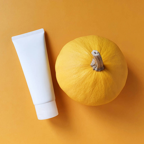 Unbranded white bottle tube for branding and label and yellow pumpkin on yellow background. Natural organic spa cosmetics concept. Vitamin intense seed of pumpkin cream concept. Mock-up - Photo, Image
