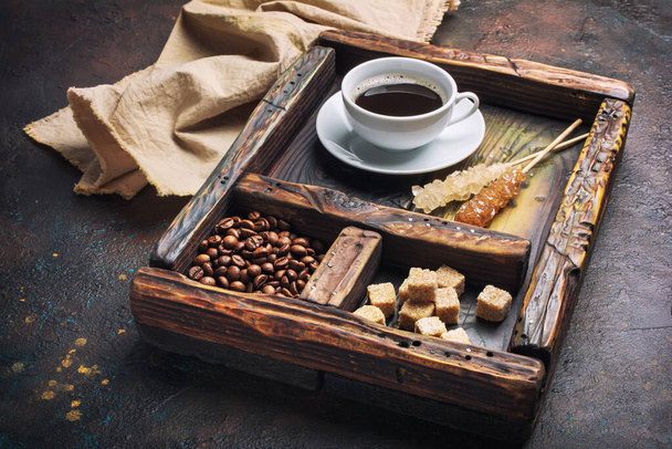 Black coffee or espresso in white cup with cane sugar crystal stick for breakfast or break on vintage woooden tray and brown background - Foto, imagen