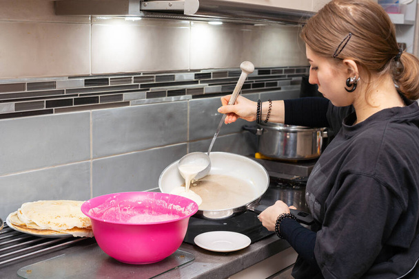 A teenage girl pours the pancake batter into a hot pan with a large spoon. Liquid pancake batter. Homemade pancakes. - Fotoğraf, Görsel