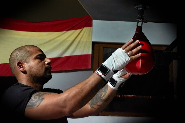 Vista lateral de boxeador masculino confiante exercitando no saco de soco no ginásio - Foto, Imagem