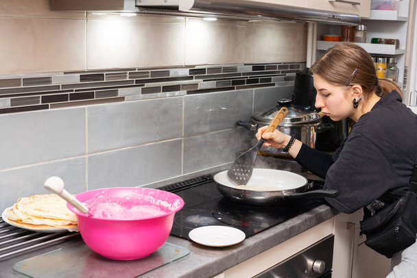 A teenage girl pricks up a partially baked pancake with the kitchen spatula and prepares to turn it over. Homemade pancakes. - Valokuva, kuva