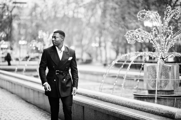 Portrait of young and handsome african american businessman in suit walking on cemter of city with garlands. - Zdjęcie, obraz