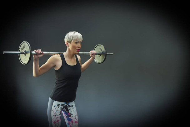 Ajuste mujer joven en ropa deportiva sonriendo mientras levanta pesas durante una sesión de entrenamiento en un gimnasio - Foto, imagen