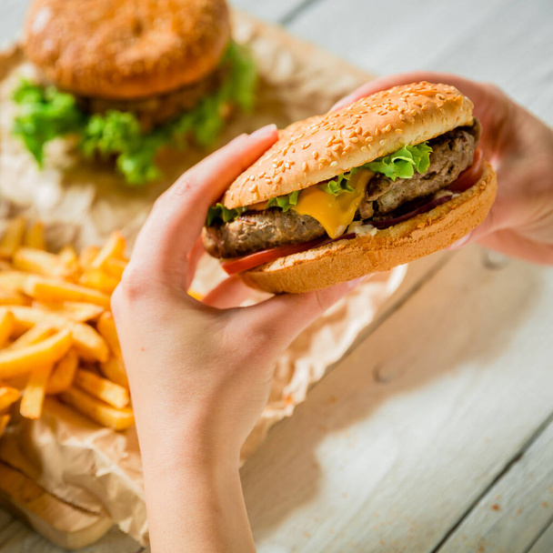 Hands and delicious burger with meat, french fries, sauce on the wooden table - Photo, Image