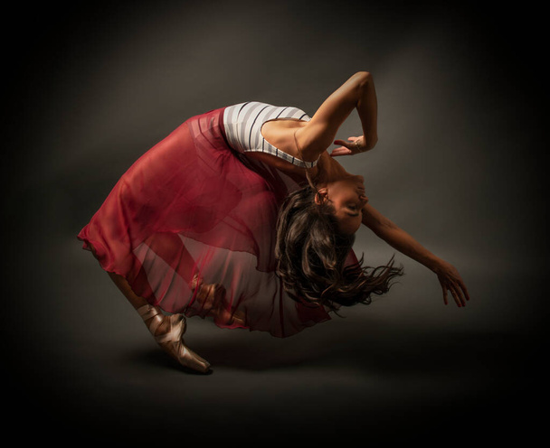 Μπαλαρίνα. Νεαρή χαριτωμένη χορεύτρια μπαλέτου, ντυμένη με επαγγελματική στολή, παπούτσια και κόκκινη φούστα χωρίς βάρος επιδεικνύει χορευτικές ικανότητες. Ομορφιά του κλασικού μπαλέτου - Φωτογραφία, εικόνα