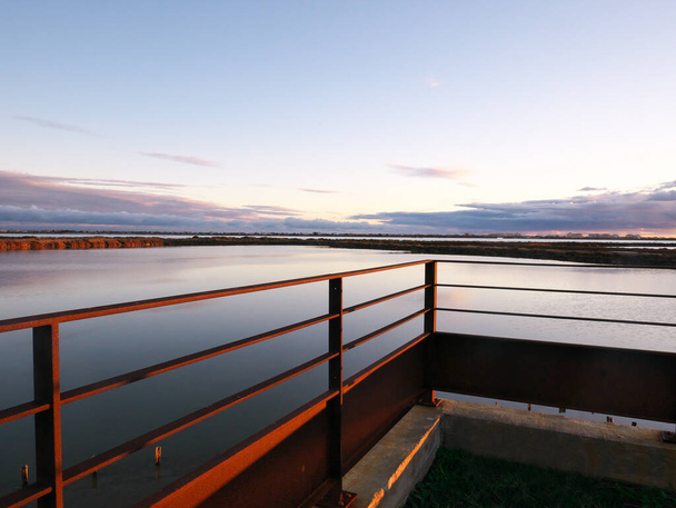 Photo prise depuis une terrasse surplombant un étang au coucher du soleil. - Photo, image