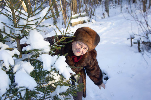 A woman in a fur hat and a fur coat made of natural fur on a fishing rod is standing near the Christmas tree, smiling and playing. Fashion in Russia in winter - Fotografie, Obrázek