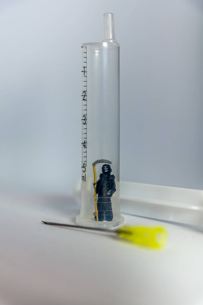 Smrtící figurka s kosou v jednorázové injekční stříkačce s jehlou vedle sebe v konceptu lékařské úmrtnosti a smrti, kopírovací prostor pod - Fotografie, Obrázek