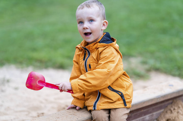 Předškolák sedí v pískovišti, hraje si s růžovou hračkou Shovel - Užijte si hřiště - Fotografie, Obrázek