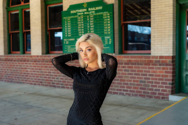 A gorgeous young blonde model poses outdoors while waiting for a train at a train depot - Fotografie, Obrázek