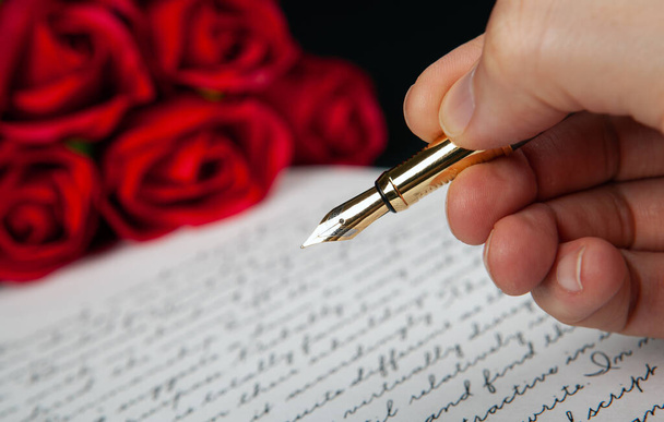 перо в руке на букву с текстом и красными розами крупным планом - Фото, изображение