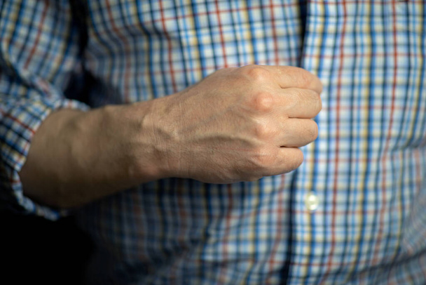 Ο άνθρωπος κουμπώνει κουμπιά στο καρό του πουκάμισο με το δεξί χέρι. - Φωτογραφία, εικόνα