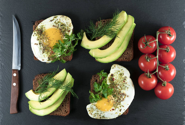 Broodjes met avocado, spinazie en gebakken eieren op een zwarte achtergrond - Foto, afbeelding