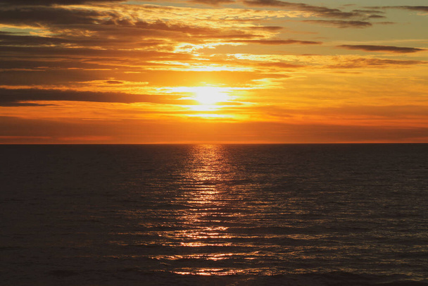 Oranssi auringonlasku horisontin yli kääntyen pilvinen taivas kaunis meri etualalla - Valokuva, kuva