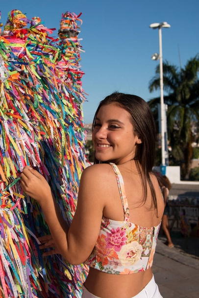 Дівчина робить запити і зав'язує кольорові стрічки на сітці перед церквою Бонфіма в Сальвадорі Баїя Бразилія. - Фото, зображення
