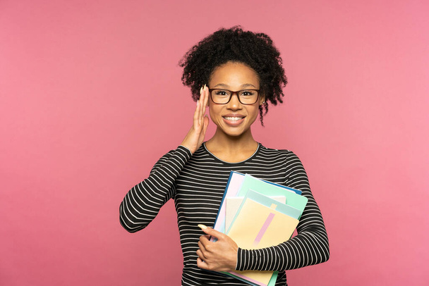 Giovane felice afro-americano tutor o insegnante donna isolata su parete rosa studio. Studente ragazza indossare occhiali che tengono quaderni e sorridente. Educazione al liceo universitario concetto di college. Spazio libero. - Foto, immagini