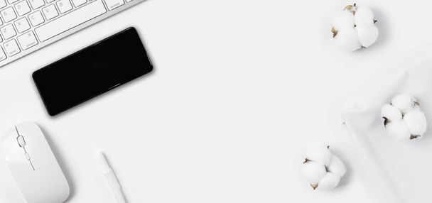 Minimale Bürotischplatte mit Tastaturcomputer, Maus, weißem Stift, Baumwollblumen, Smartphone, weißem Stoff auf weißem Tisch mit Kopierraum, Komposition am Arbeitsplatz in weißer Farbe, flache Verlegung - Foto, Bild