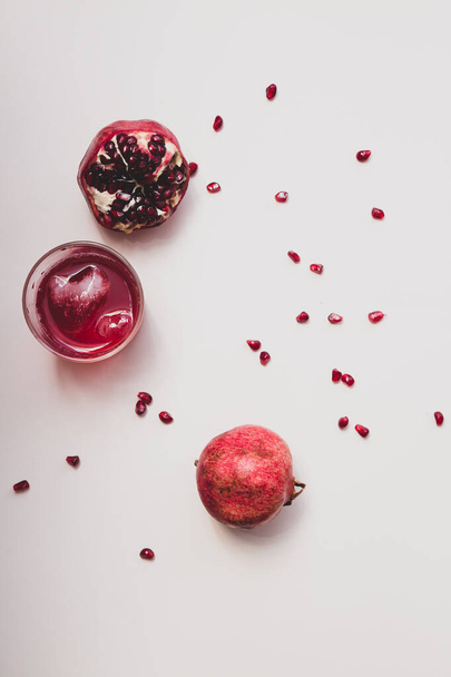 Minimalistisch stilleven met granaatappel fruit en granaatappelsap in een glazen glas met een ijsblokje in de vorm van een hart op een lichte achtergrond selectieve focus top view - Foto, afbeelding