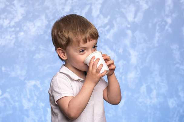 little boy drinks water from a disposable cup of cornstarch. ecologicaly clean. replacing plastic with modern biodegradable materials. child of European appearance close up - Foto, imagen