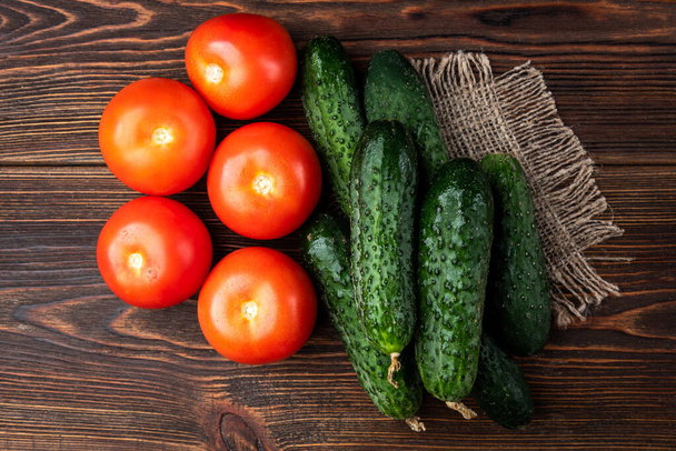 Verse komkommers en tomaten op donkere houten ondergrond - Foto, afbeelding