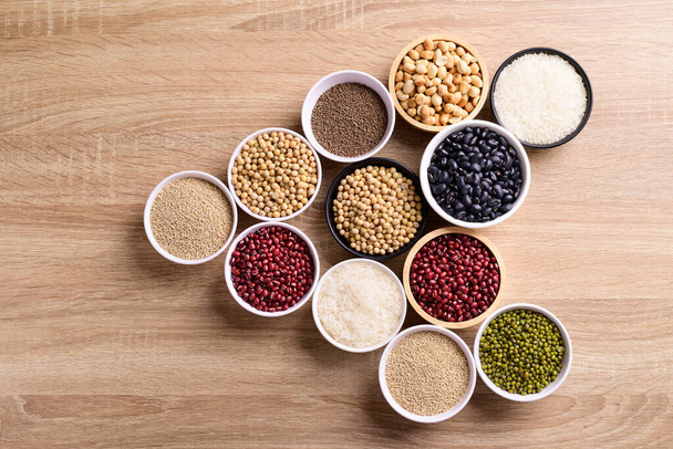 Varios cereales en un tazón sobre fondo de madera (semillas de quinua, frijol negro, cacahuete, semillas de perilla, soja, frijoles azuki, granos de arroz y frijoles mungo)) - Foto, Imagen