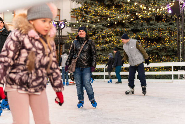 Κίεβο (Κίεβο), Ουκρανία - 27 Δεκεμβρίου 2020: Πολλοί χαρούμενοι άνθρωποι και παιδιά κάνουν πατινάζ στον πάγο έξω κοντά στο Γραφείο (Διοίκηση) του Προέδρου της Ουκρανίας - Φωτογραφία, εικόνα
