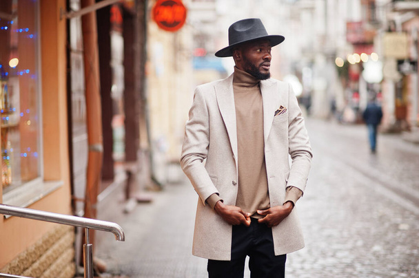 Stylish african american man wear beige jacket and black hat pose at street. - Photo, Image