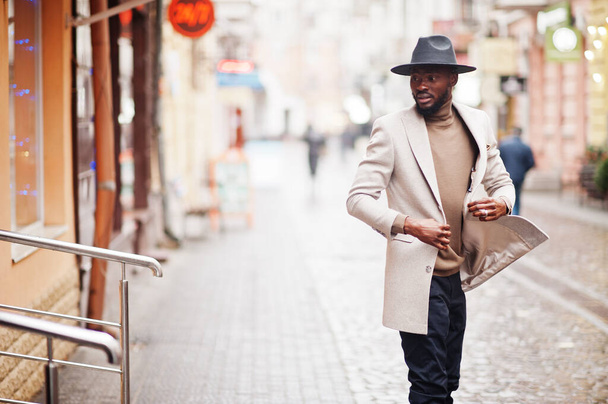 Stylish african american man wear beige jacket and black hat pose at street. - Fotó, kép