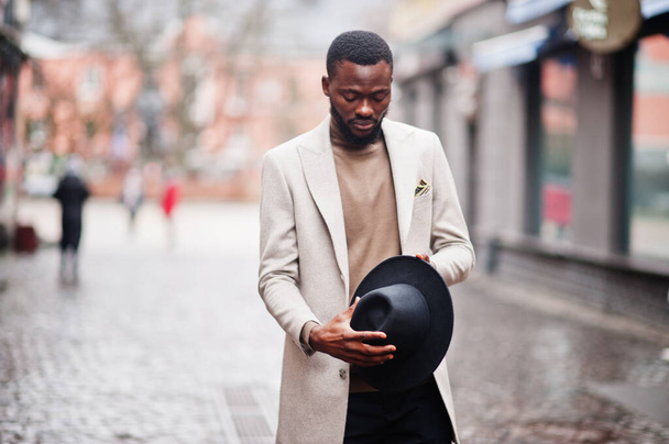 Stylish african american man wear beige jacket and black hat pose at street. - Фото, изображение