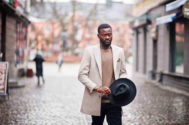 Stylish african american man wear beige jacket and black hat pose at street. - Фото, изображение