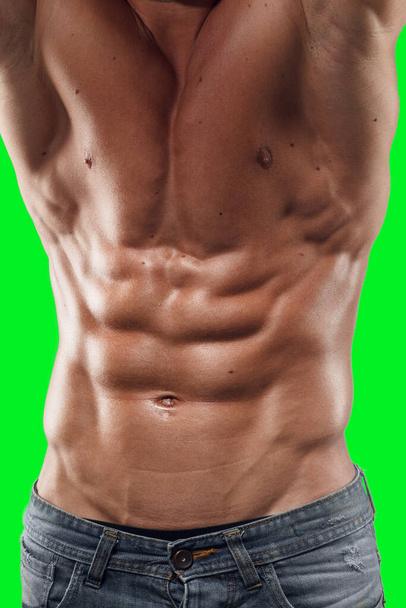Крупный план спортивного молодого человека, с тонированным телом, позирующим в рубашке и смотрящим вниз, изолированным на зеленом фоне. - Фото, изображение