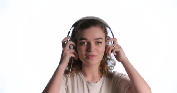 Mujer feliz poniéndose auriculares, escuchando música y bailando sobre fondo blanco aislado - Metraje, vídeo