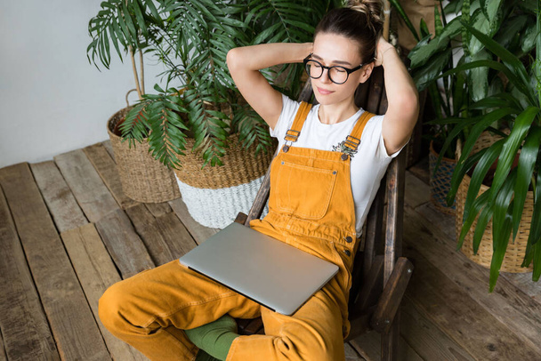 Female gardener put hands behind head feels placidity, resting after work, sitting on wooden chair in home garden, closed eyes, laptop on her knees.Break during work.No stress anxiety fatigue relief  - Photo, Image