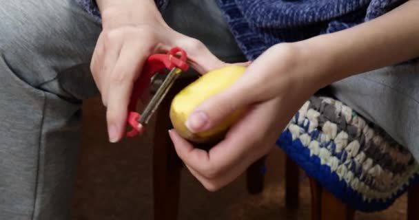 Mulher descasca batatas enquanto se senta em uma cadeira na cozinha - Filmagem, Vídeo