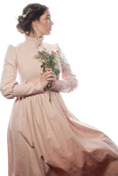 Young brunette woman in pink dress holding a bouquet of roses and dreaming of love over white background - Foto, afbeelding